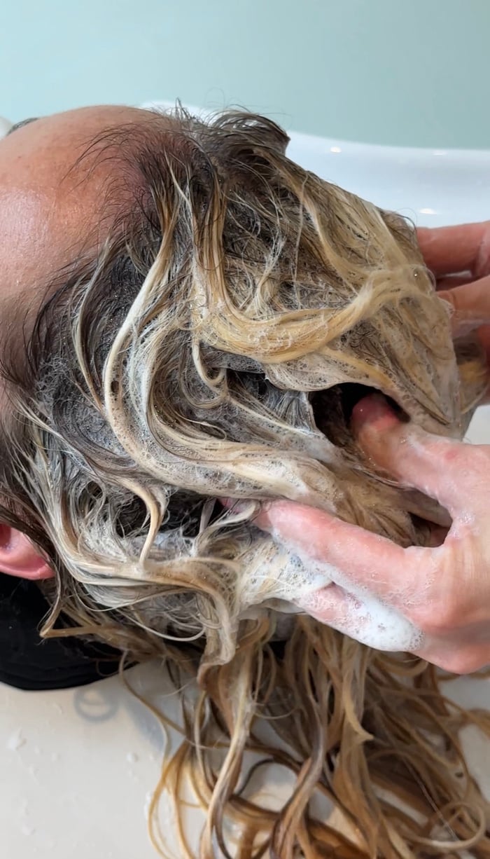 Coloristin arbeitet Gloss und Toner in nasses blondiertes Haar ein