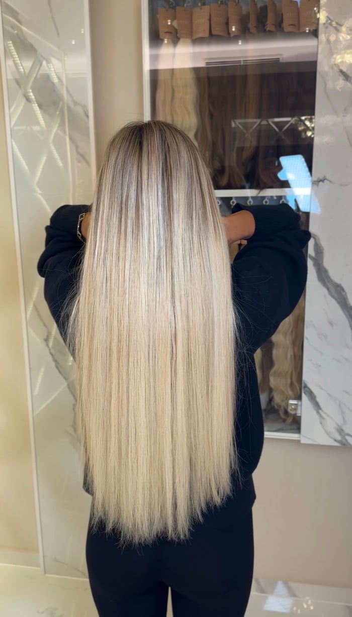 Sehr lange glatte blonde Balayage Extensions in Rückansicht vor dem Spiegel