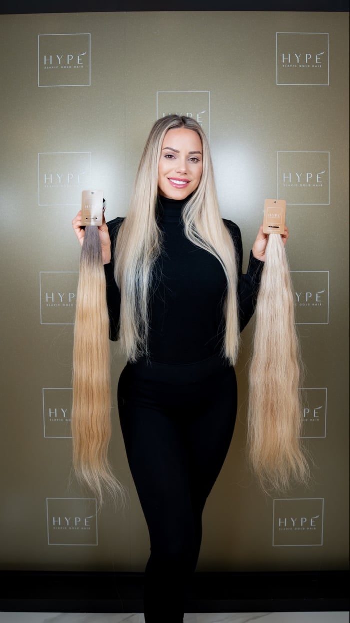 Model hält zwei extra lange blonde Slavic Gold Hair Strähnen vor der HYPE Fotowand