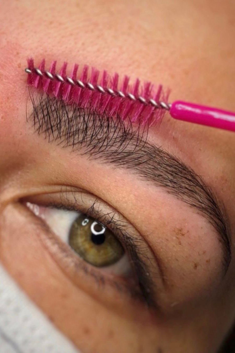 Augenbraue wird mit pinkem Spoolie vor der Powder-Brows-Behandlung ausgebürstet
