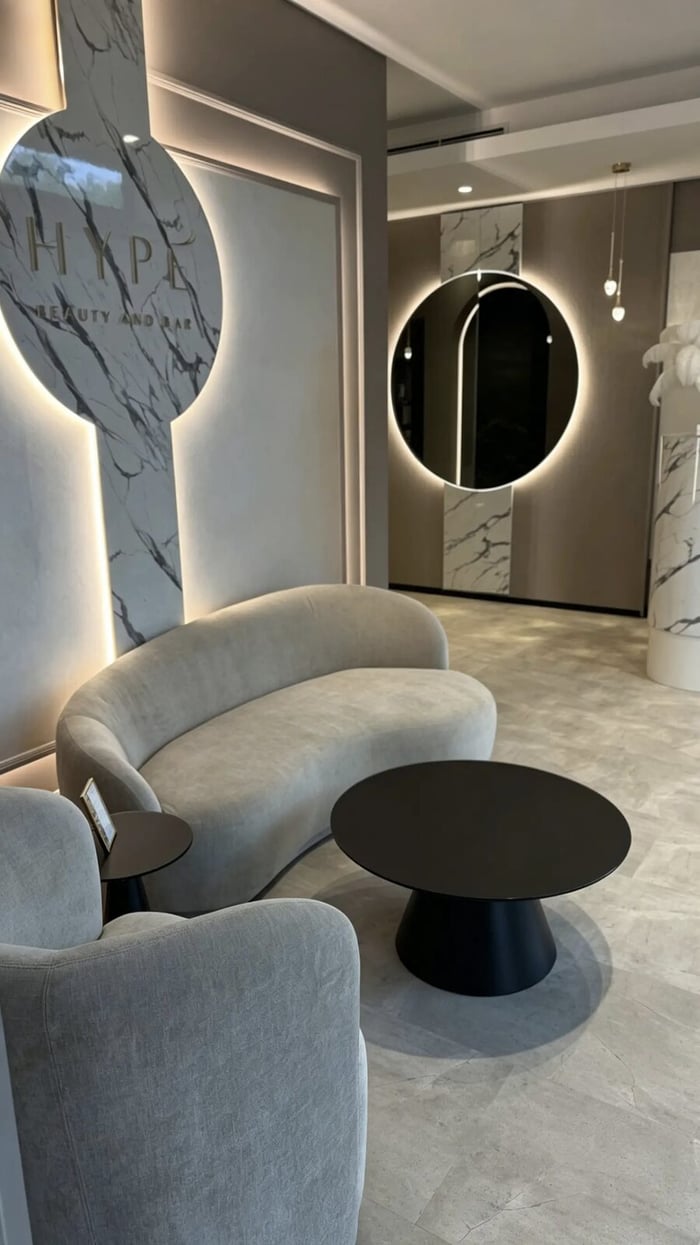 Lounge mit Rundspiegel, Federlampe und Marmorsäule bei HYPE Beauty & Bar