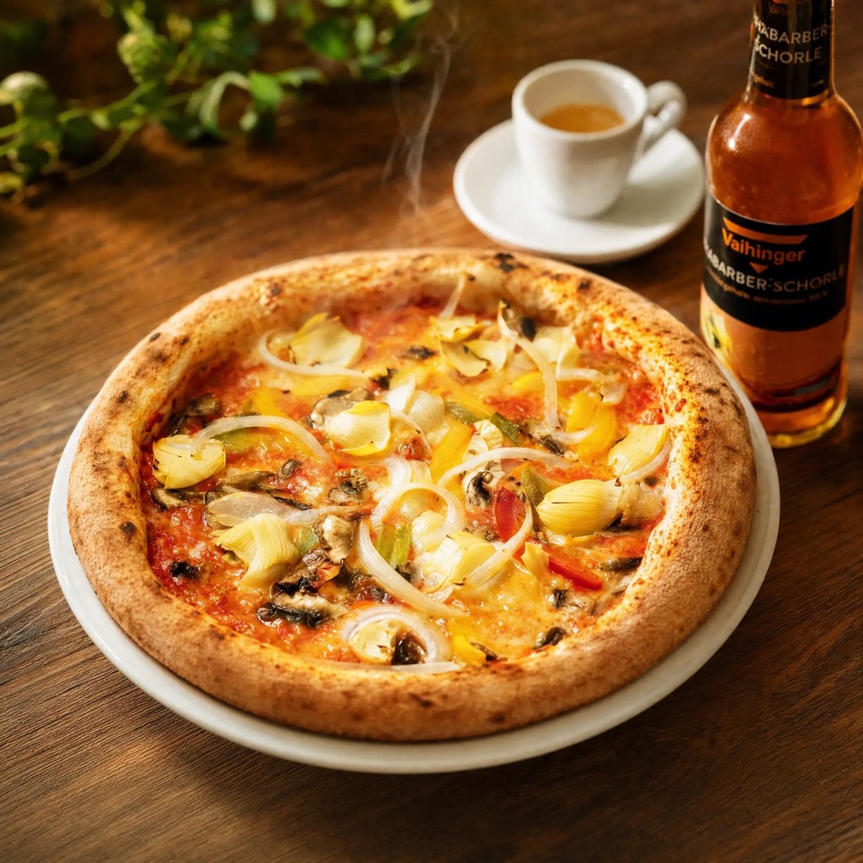 Pizza mit Artischocken, Paprika, Champignons und Zwiebeln, daneben ein Espresso und eine Flasche Rhabarberschorle