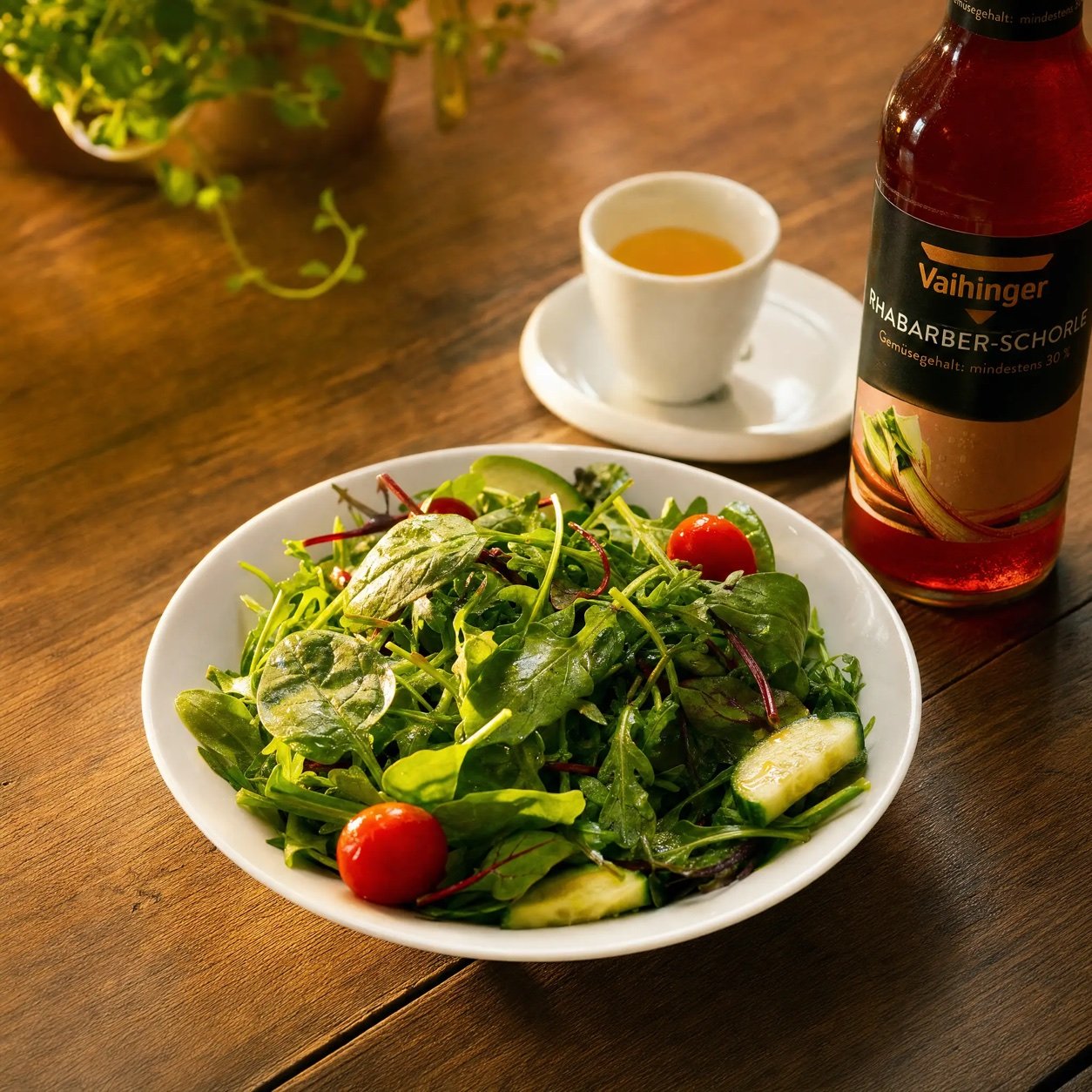 Gemischter Blattsalat mit Rucola, Kirschtomaten und Gurke, daneben Dressing und eine Flasche Rhabarberschorle