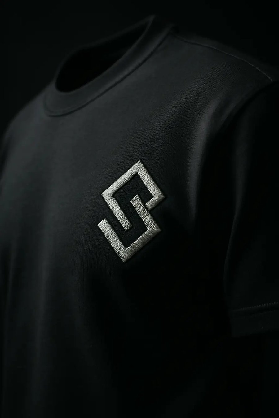 Editorial-Nahaufnahme einer monochromen Logo-Stickerei auf schwarzem Premium-Tee