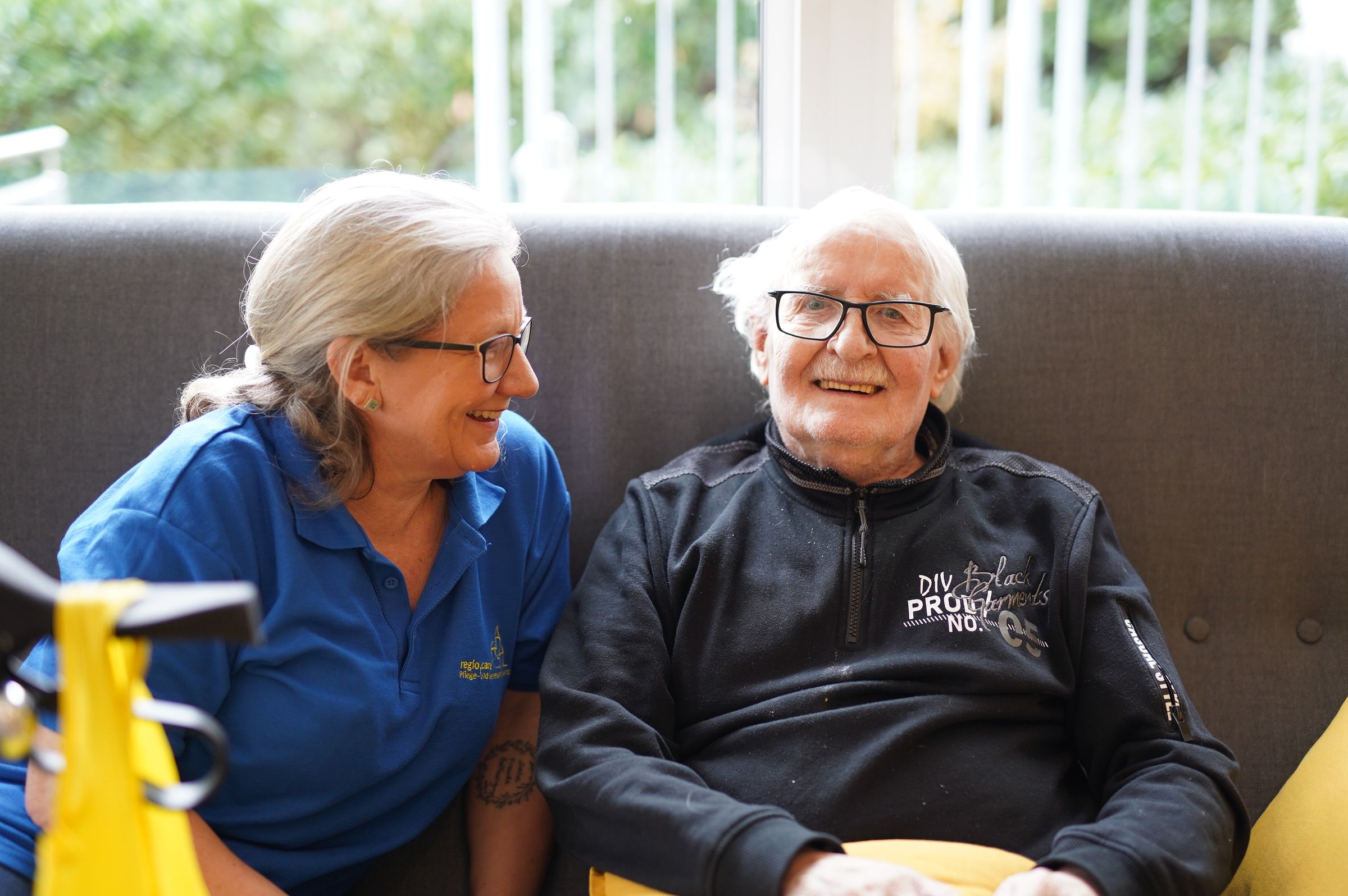 Pflegekraft der regio.care im Gespräch mit einem Senior auf dem Sofa