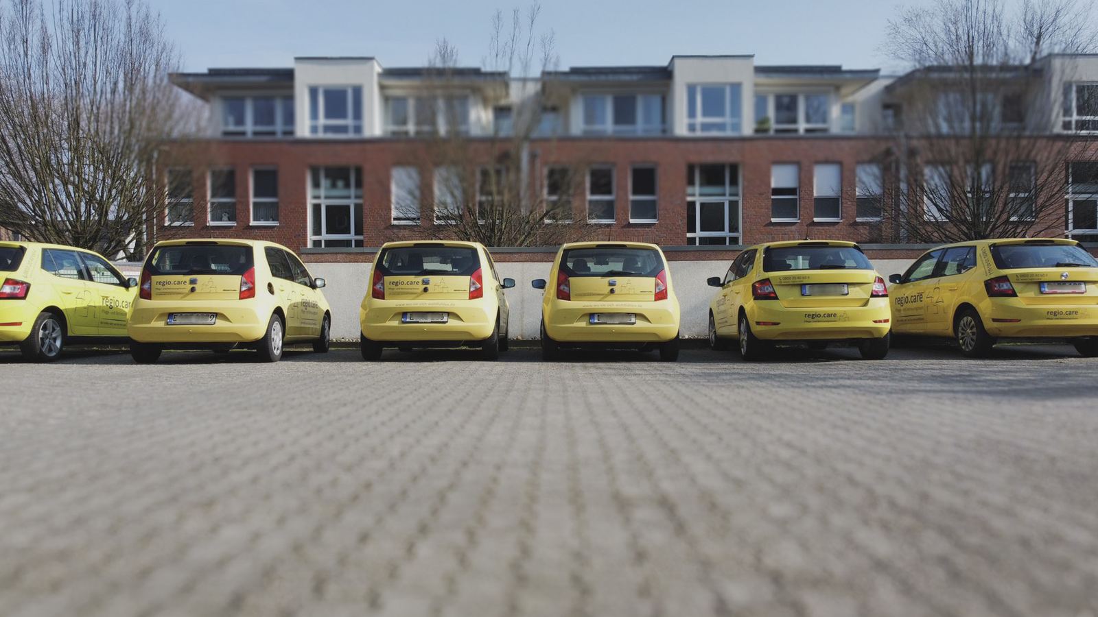 Gelbe Dienstwagen der regio.care vor einem Bürogebäude