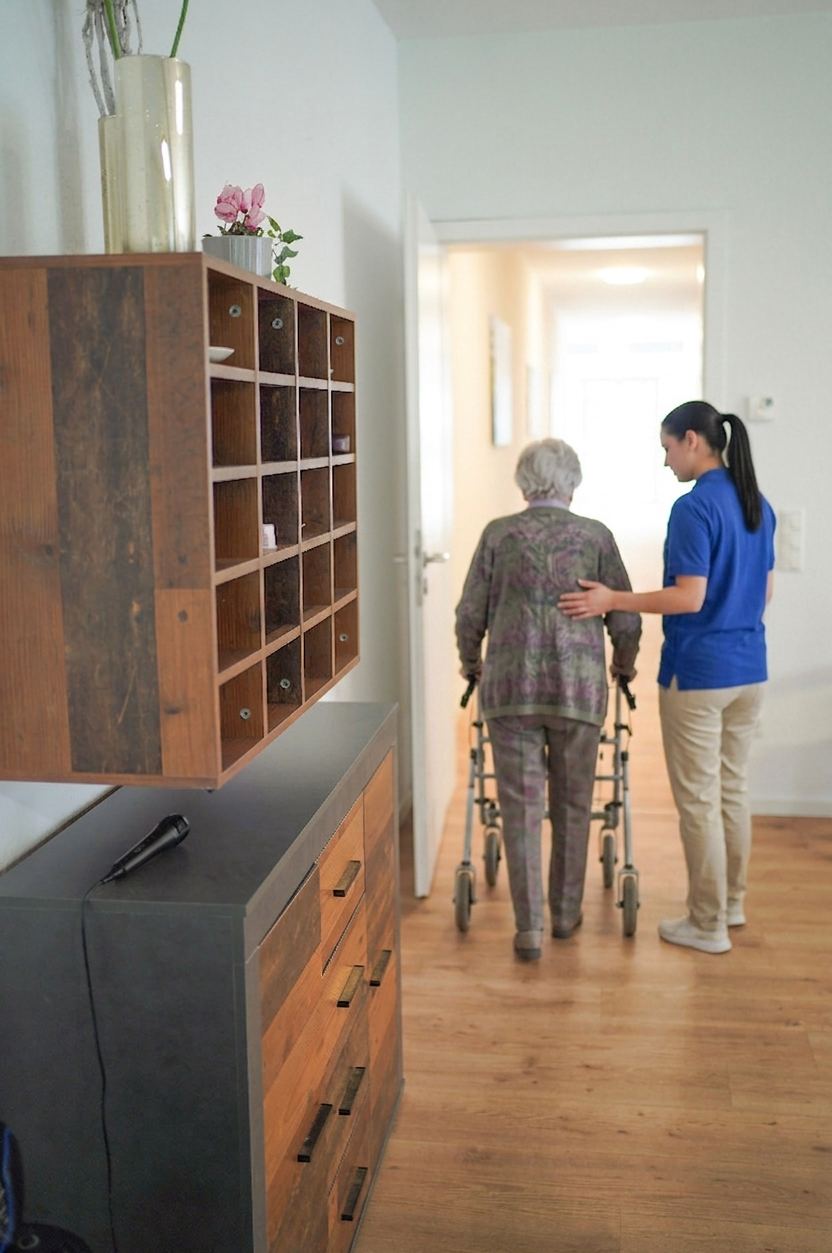 Mitarbeiterin begleitet eine Seniorin mit Rollator