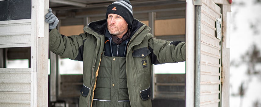 Man wearing insulated work bib overalls and an insulated jacket works on a ranch in the winter.