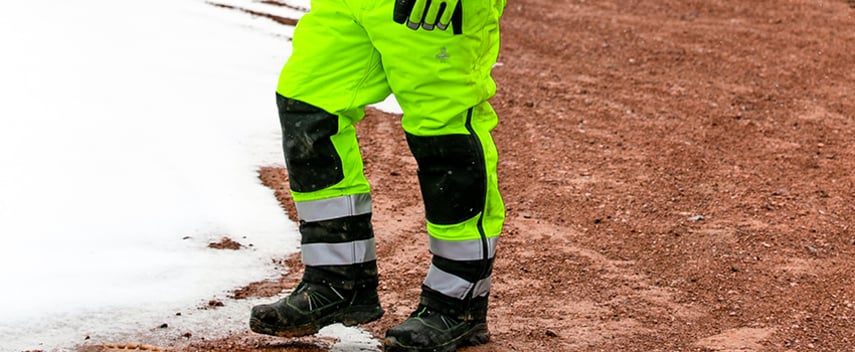 Construction worker wearing high-visibility insulated work pants stands on a winter jobsite.
