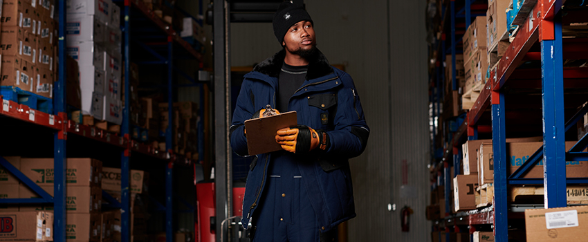 Man working in a cold climate-controlled warehouse wears insulated  bib overalls and a work jacket.