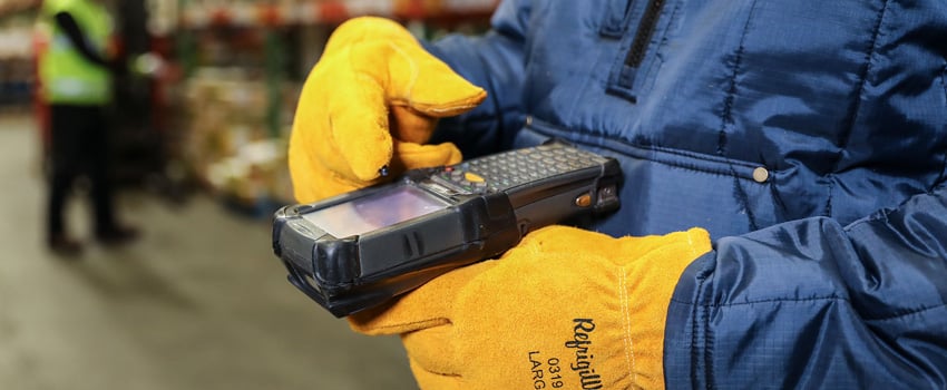 Person wearing Key-Rite insulated work gloves uses a handheld scanner keypad in a refrigerated warehouse.