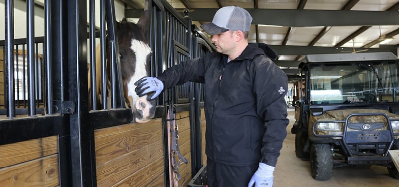Man petting a horse in a barn wearing RefrigiWear