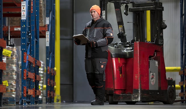 Man works in a refrigerated warehouse  while wearing an insulated freezer suit, insulated work boots and high-dexterity gloves.