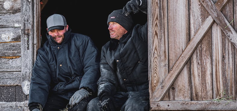 2 men sitting on a barn in the cold wearing RefrigiWear gear to stay warm