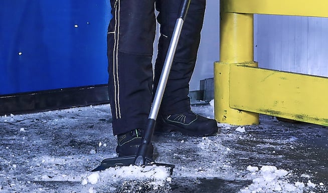 Person in a cold storage warehouse  shovels ice while wearing non-slip freezer boots.