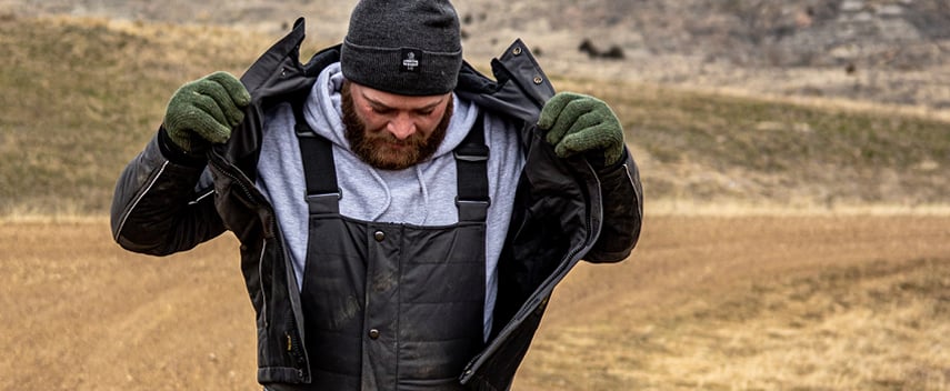 Man working outside in the cold removes an outer layer to prevent over insulation while he's very active.