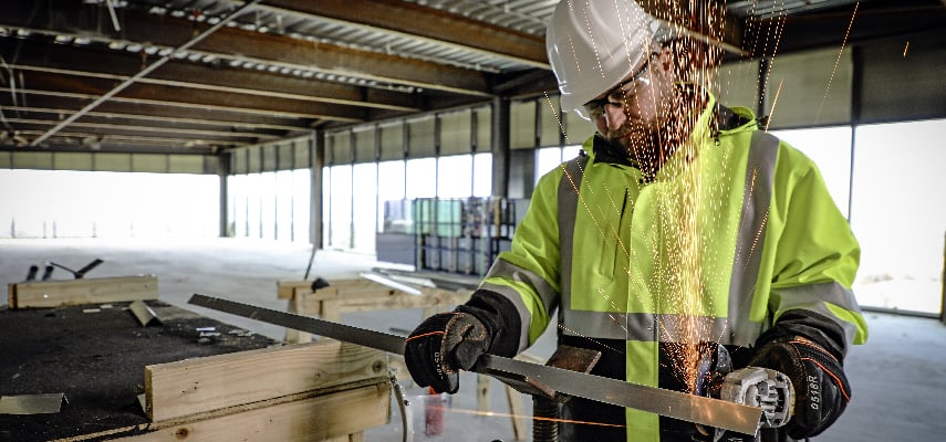 Man working on roofing for a commercial building wears a high-visibility insulated work coat for winter.