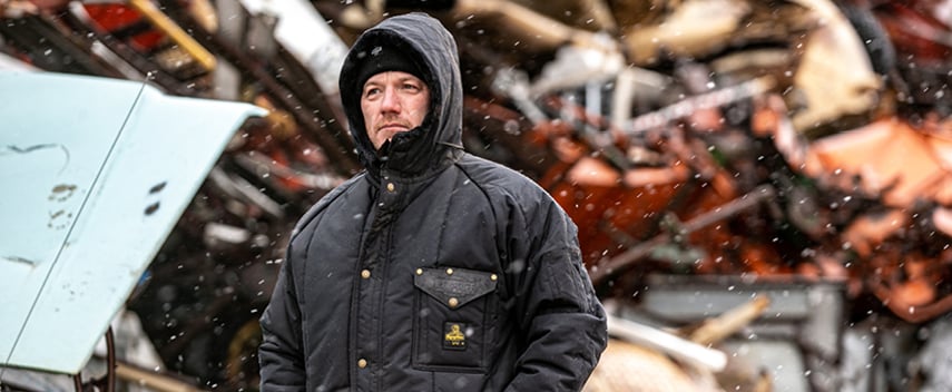 Man wearing an insulated work coat with hood blocks out the wind and snow.