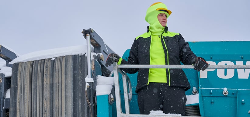 Woman in insulated high-visibility workwear for women standing on heavy equipment in snowy conditions, showcasing female PPE built for tough winter jobs.
