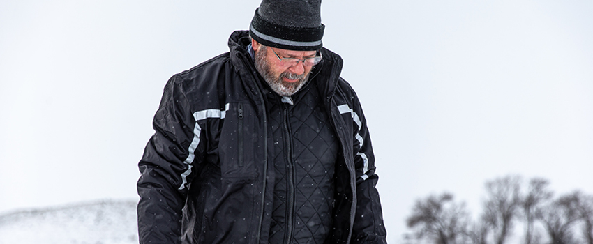 Man working in the snow wears a base layer, mid-layer jacket and waterproof overcoat to stay warm.