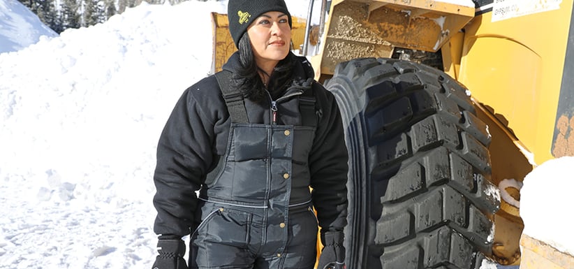 Woman wearing women's insulated bib overalls next to  a tractor in the snow.