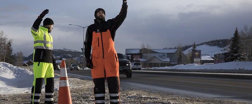 Men wearing insulated bib overalls and cold weather work jackets direct traffic on a job site.