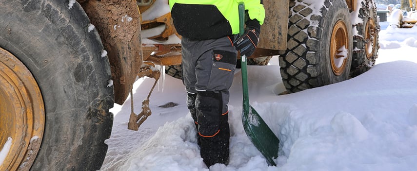 Construction worker wearing insulated work pants shovels snow on a jobsite.