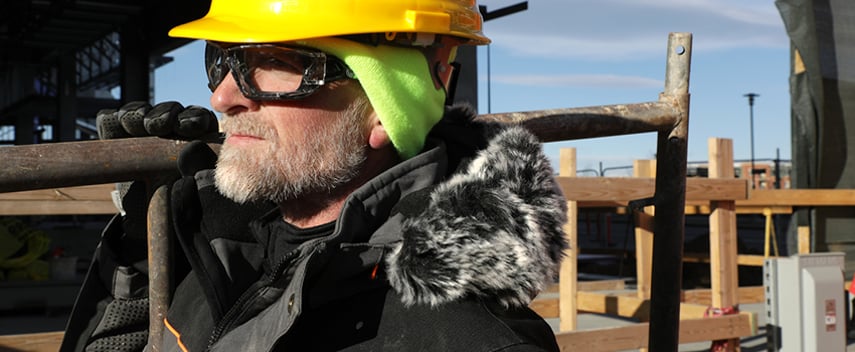 Man wears insulated work jacket and a beanie under a hard hat.