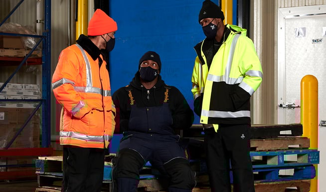 People wearing insulated work jackets and freezer suits work in a refrigerated warehouse.