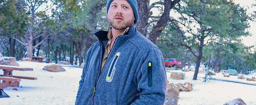 Man camping in the woods wears a fleece jacket and knit cap.