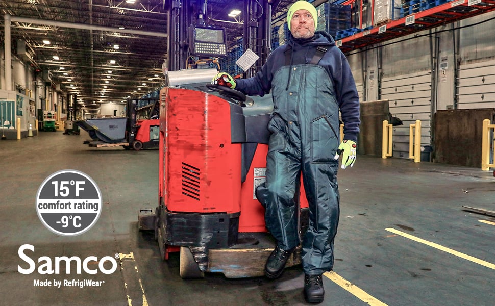 Man standing in a cold storage facility wearing the Econo-Tuff High Bib overalls in front of a forklift