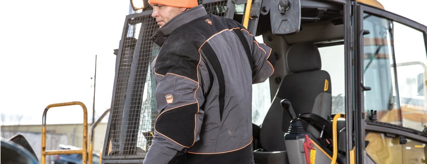 Man wearing insulated workwear with Performance-Flex stretches to climb into heavy equipment on a job site.