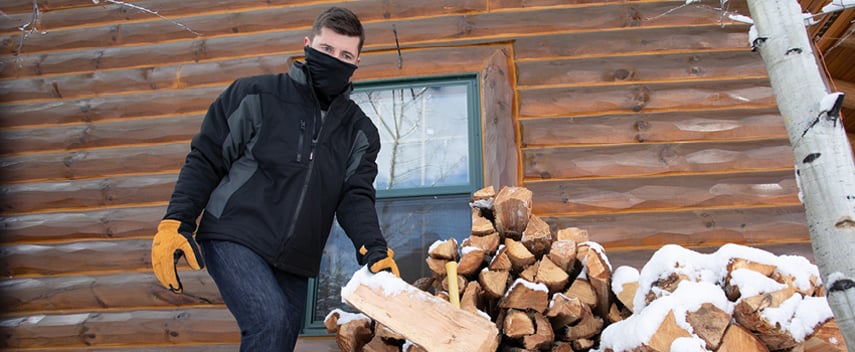 Man wearing insulated work coat and leather work gloves stacks firewood in the winter.