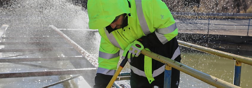 Man working outside in cold weather sprays water to clean construction equipment.