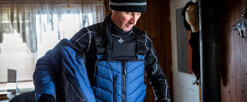 Man dresses for working in extreme cold by layering thermal underwear  under insulated overalls and a work coat.