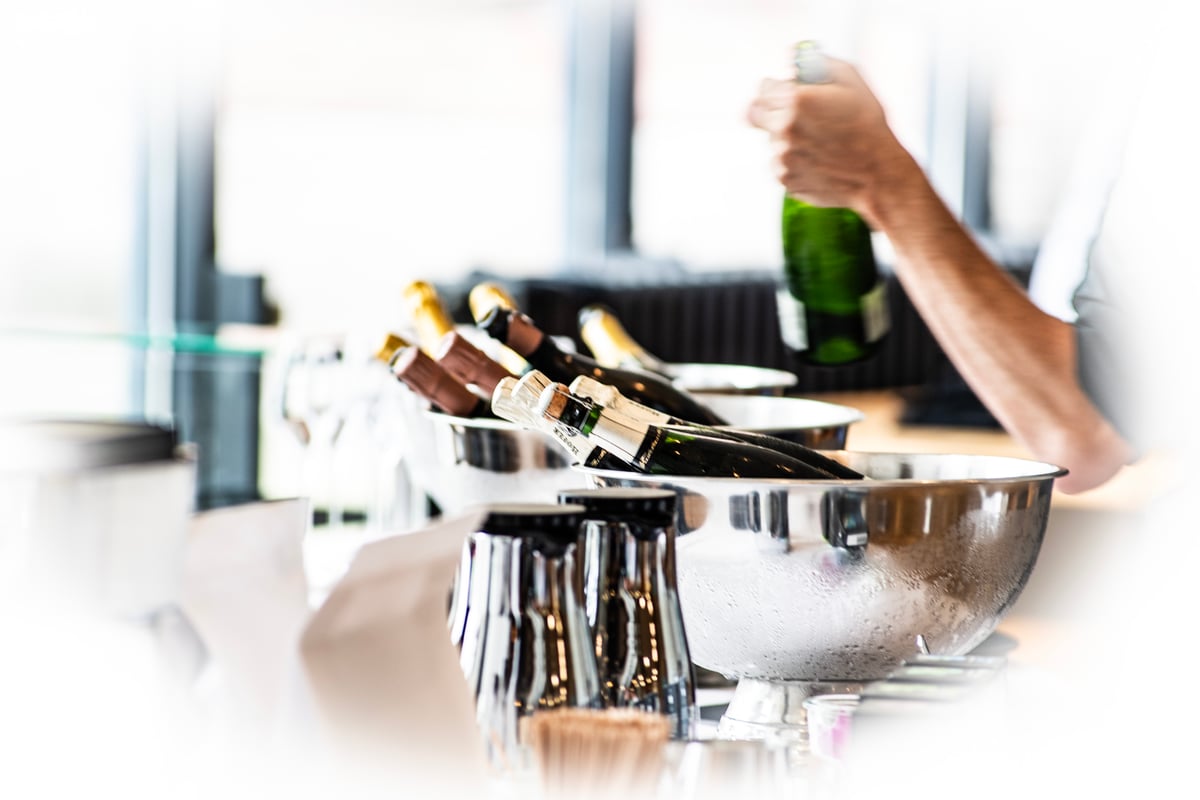 Sekt wird schwungvoll aus einem Sektkühler genommen. Das Eis sorgt für Frappee am Kühler.