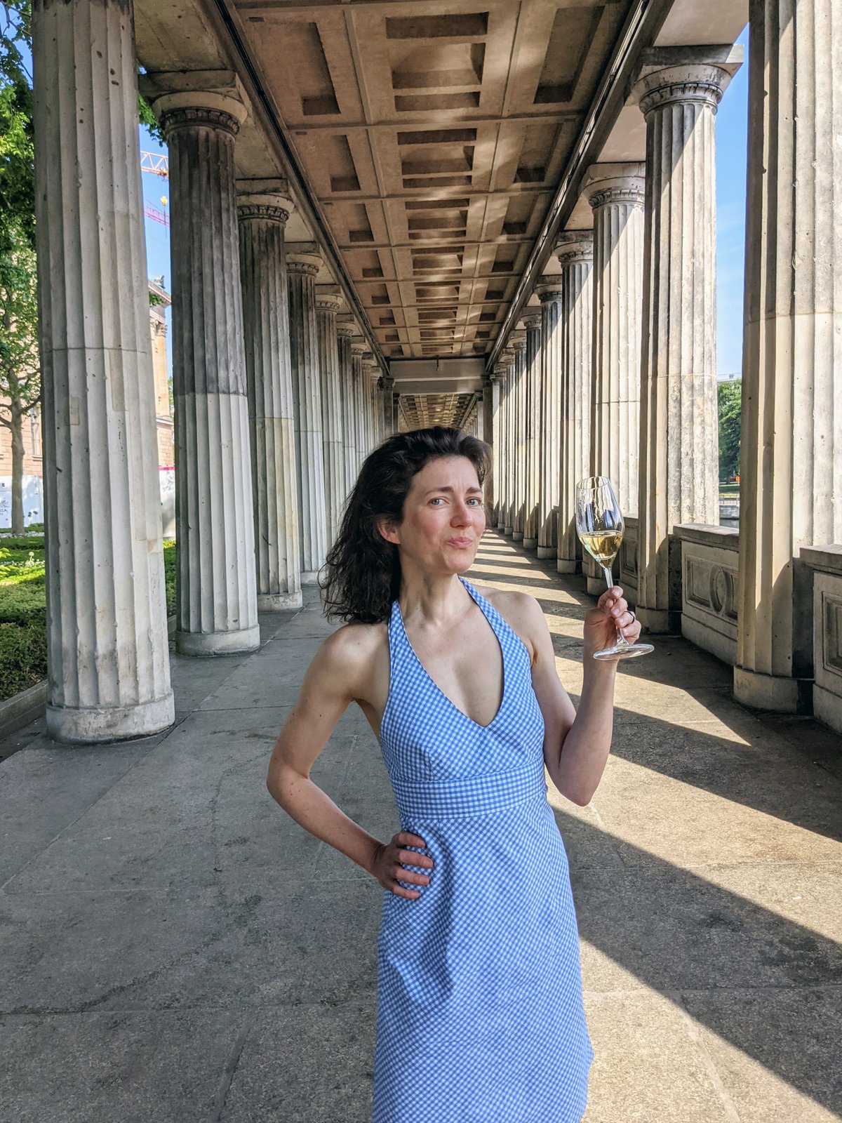 Alexandra in blau-weiß kariertem Dress auf der Berliner Museumsinsel. Säulen im Hintergrund.