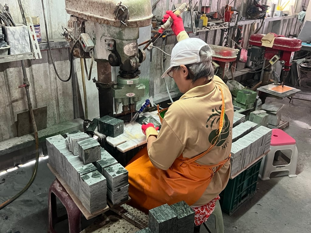 A local worker in gloves drills and polishes marble pieces at a small Hualien stone workshop