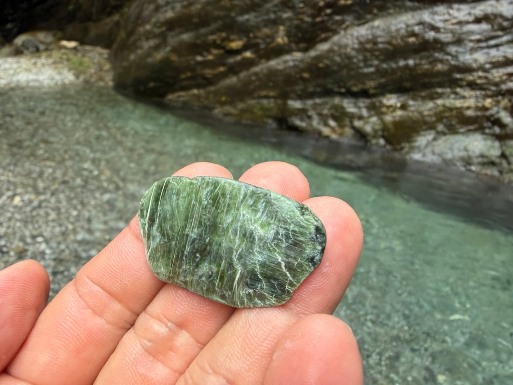 白鮑溪溯溪尋玉 ── 手中拿著一塊綠色台灣玉, 背景是清澈溪流與峽谷岩壁