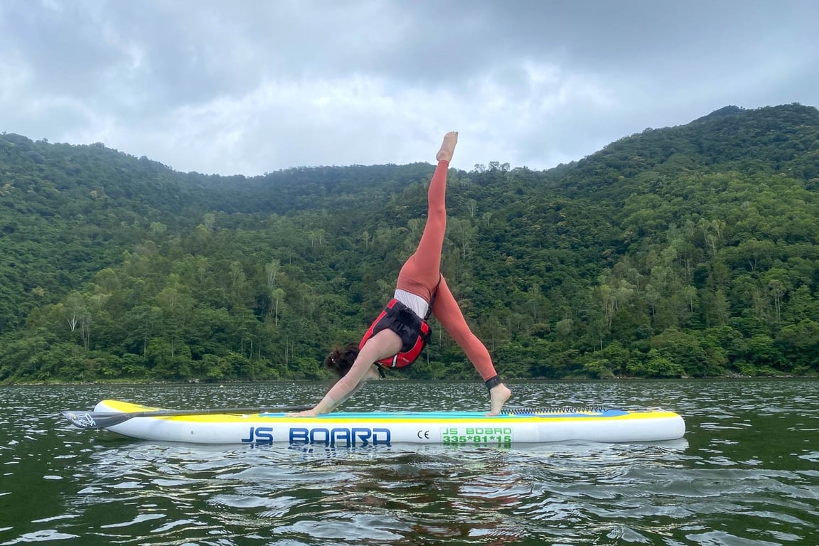 女學員在鯉魚潭 SUP 板上做瑜珈倒立, 山林湖面背景