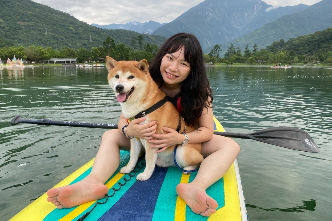 女學員與柴犬一起坐在鯉魚潭 SUP 板上, 背景是中央山脈