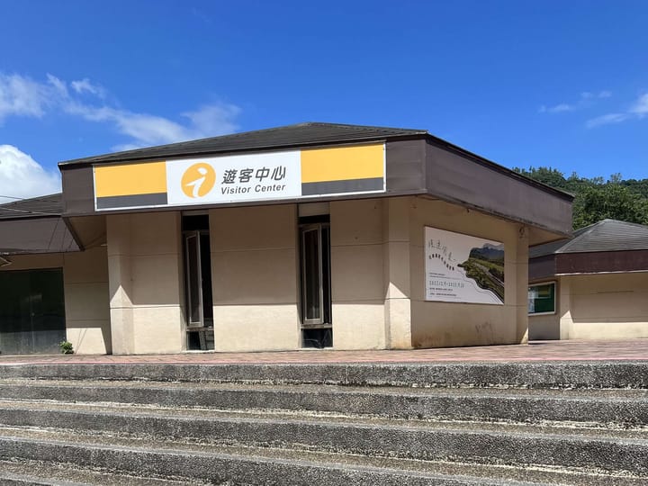 鯉魚潭遊客中心建築外觀, 黃色 i 招牌標示, 後方為中央山脈