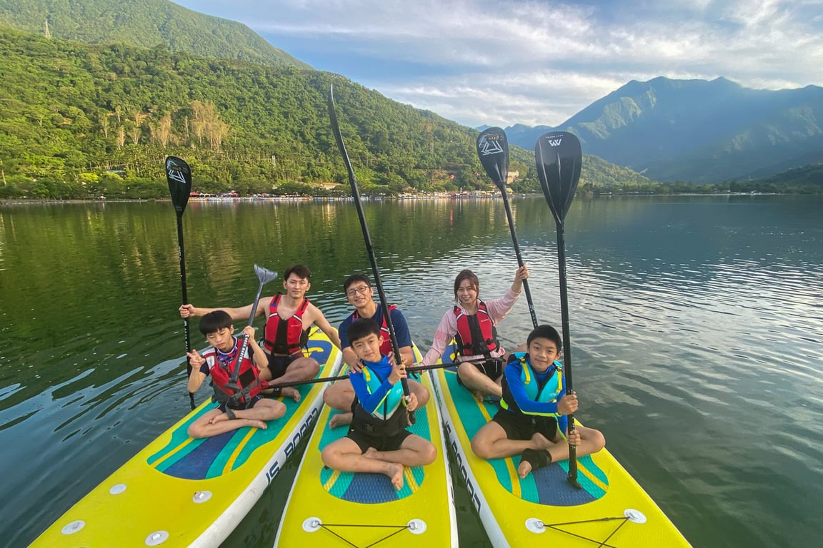 鯉魚潭 SUP 三位教練帶四位小朋友坐在板上舉槳合照, 中央山脈倒映湖面