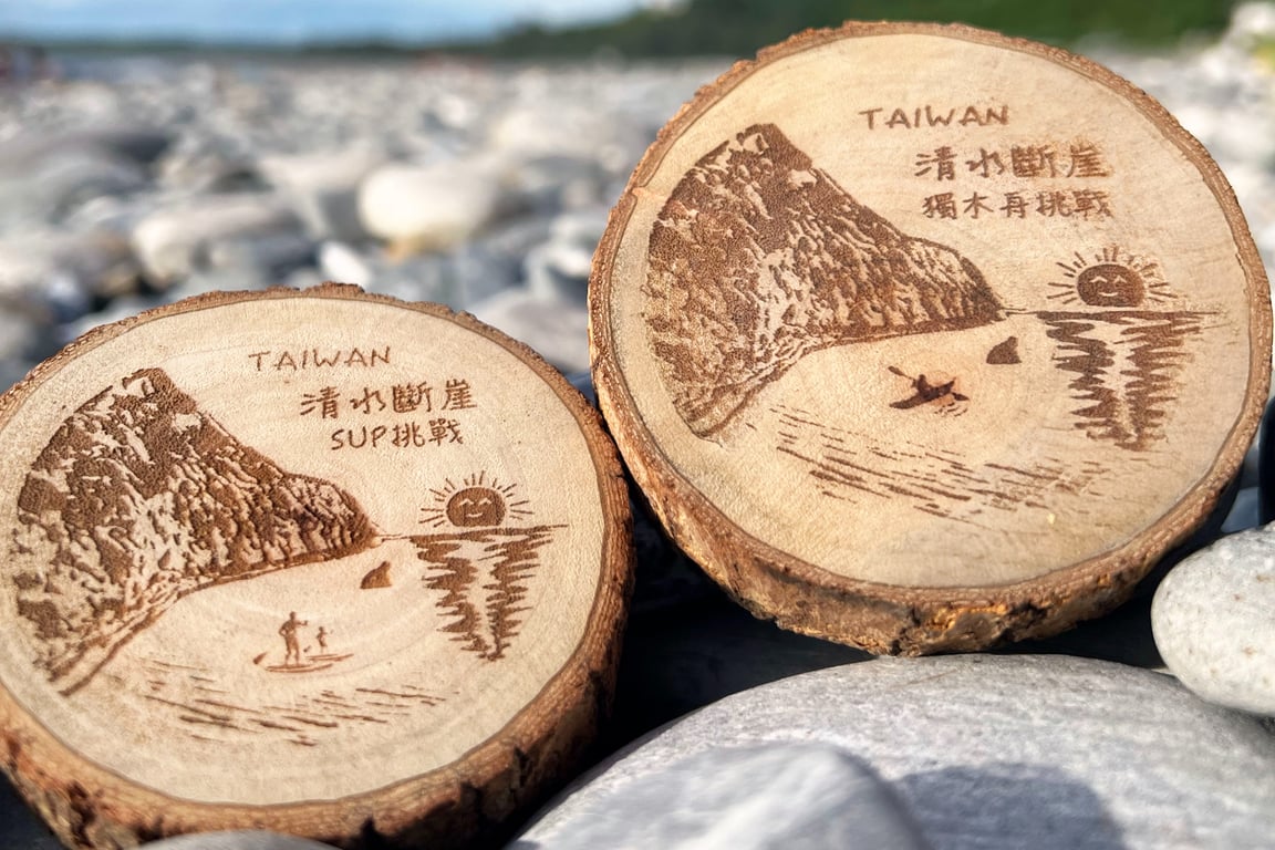 兩枚教練親手打磨的原木獎牌, 雷雕清水斷崖崖壁 + 日出, 一枚刻「SUP挑戰」、一枚刻「獨木舟挑戰」, 背景是崇德礫石灘
