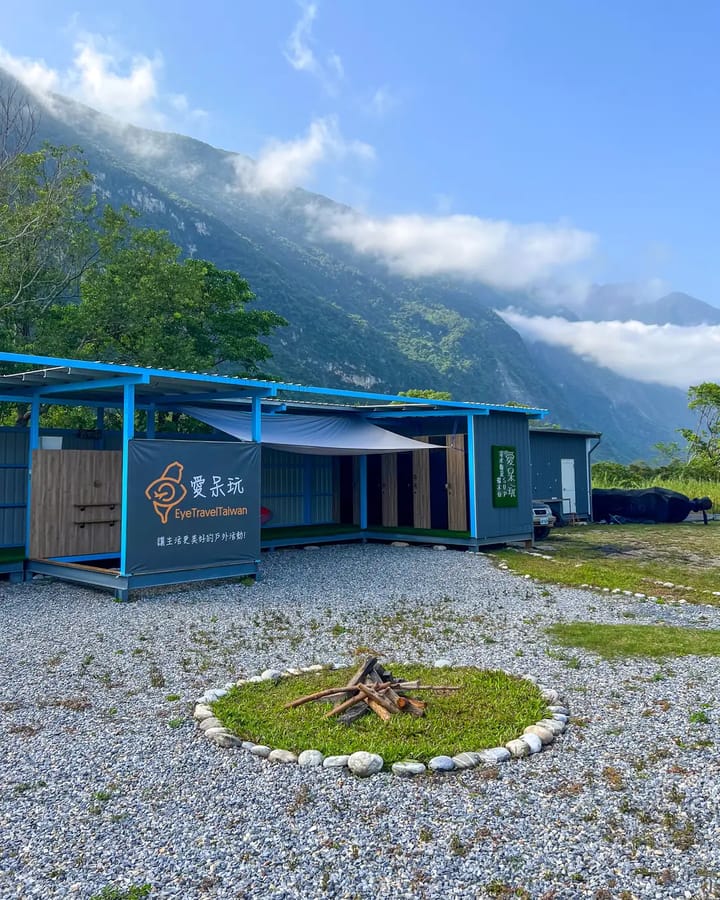 愛呆玩崇德報到基地 ── 藍色屋簷的半戶外建築, 前方有石頭圍成的營火圈, 後方是雲霧繚繞的山