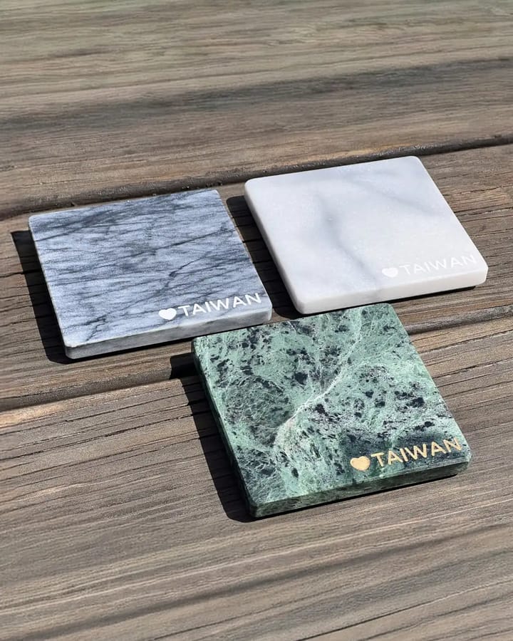 Three Hualien marble coasters — grey, white, and green — engraved with a heart and the word TAIWAN, arranged on weathered wooden planks
