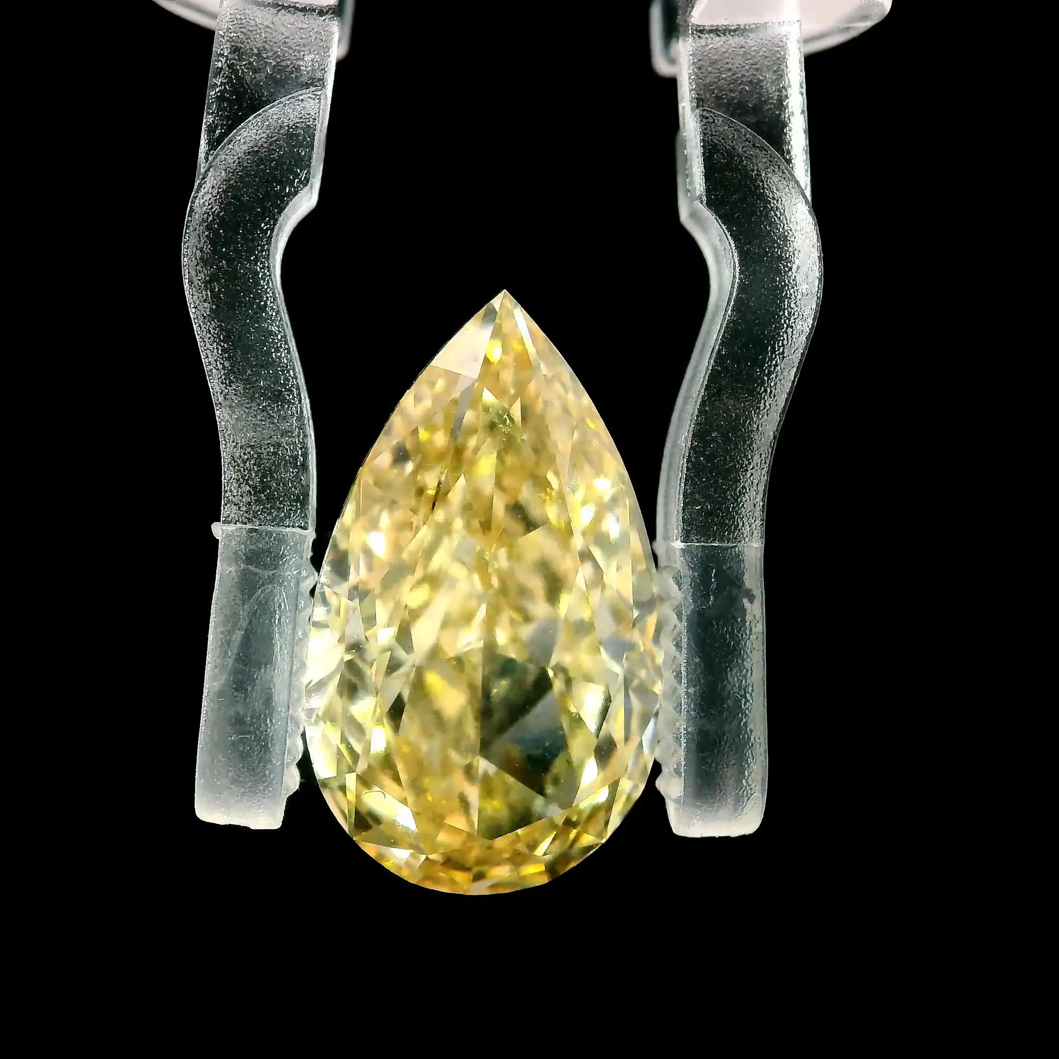 A loose pear-shaped yellow diamond on a black background held by Gem Clip 