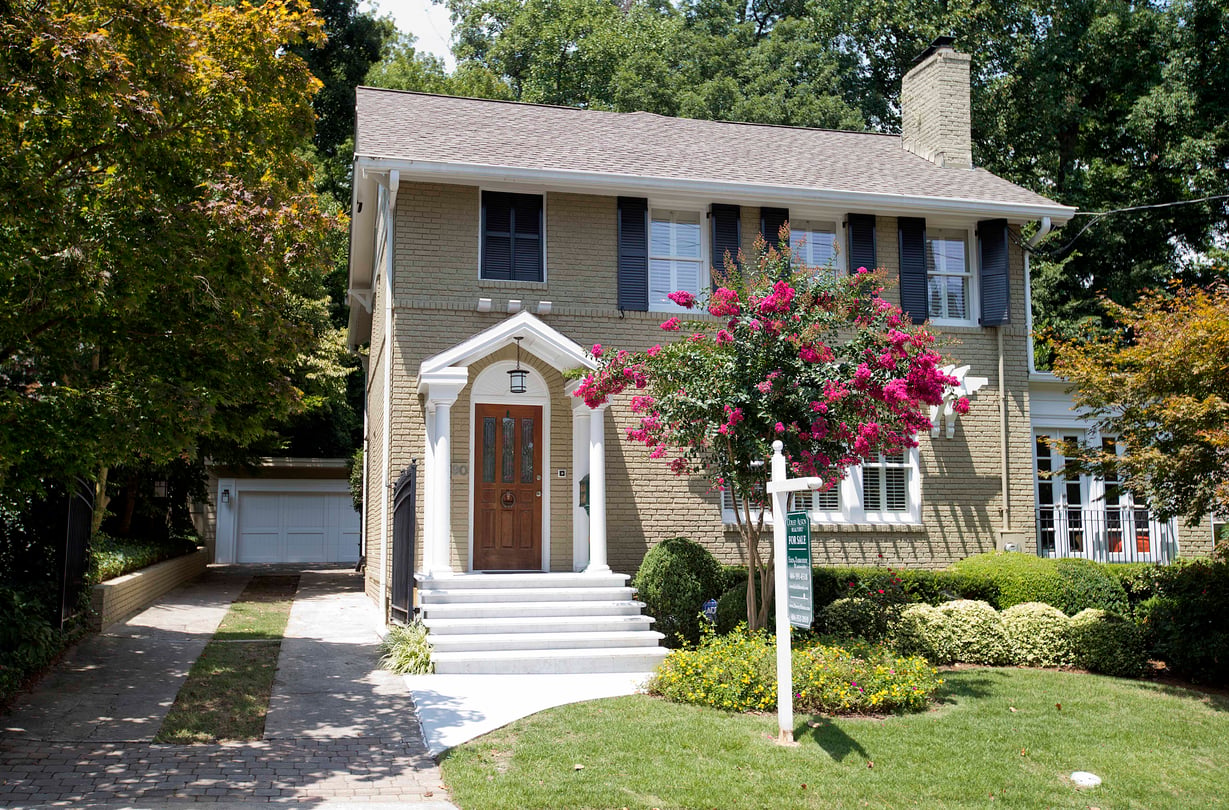 A two-story, beige home with a dark wood door and dark grey shutters in Sherwood Forest neighborhood in Atlanta.
