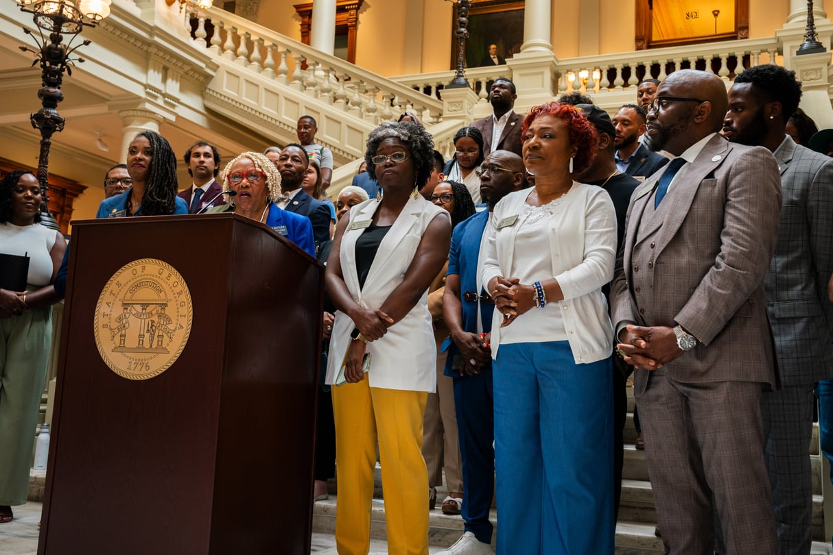 A group of teachers and advocates stand behind a podium at the Georgia State Capitol