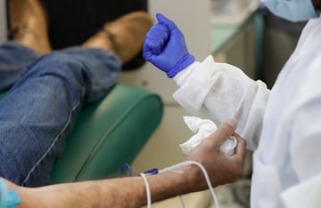 A phlebotomist makes a fist to instruct a patient to make a fist before he donates blood.